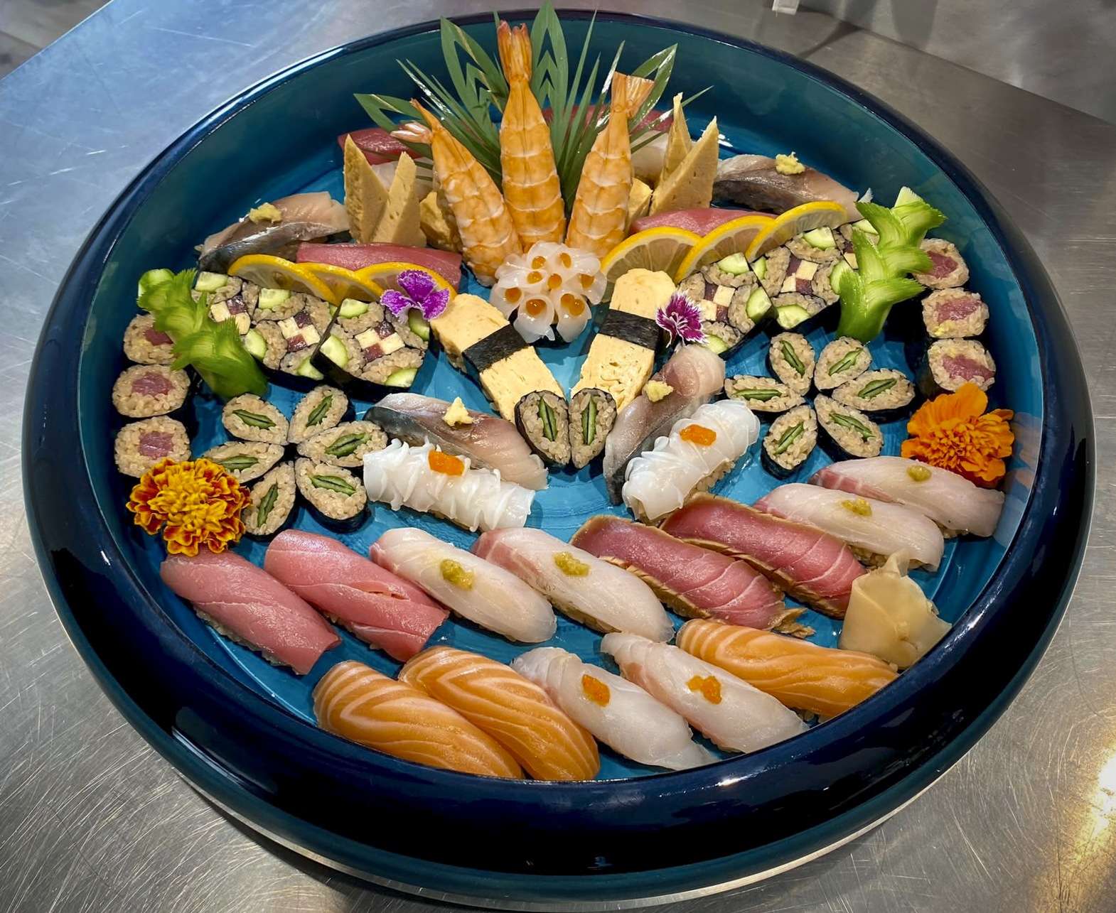 Bandeja redonda azul con un mosaico de nigiris de atún rojo, salmón, tamago, hamachi y langostinos
