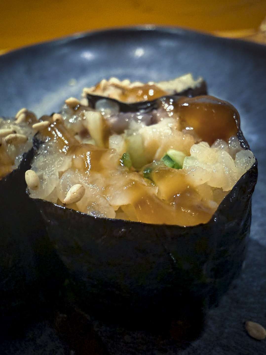 Maki de anguila envuelto en alga nori con salsa sukiyaki, sobre un plato de piedra