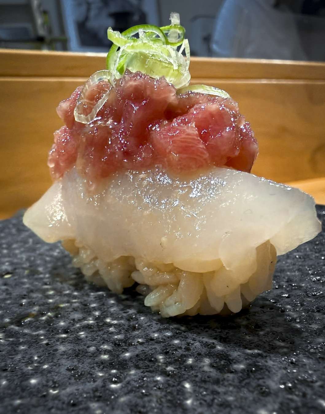 Primer plano de un nigiri de vieira coronado con tartar de chutoro y brotes