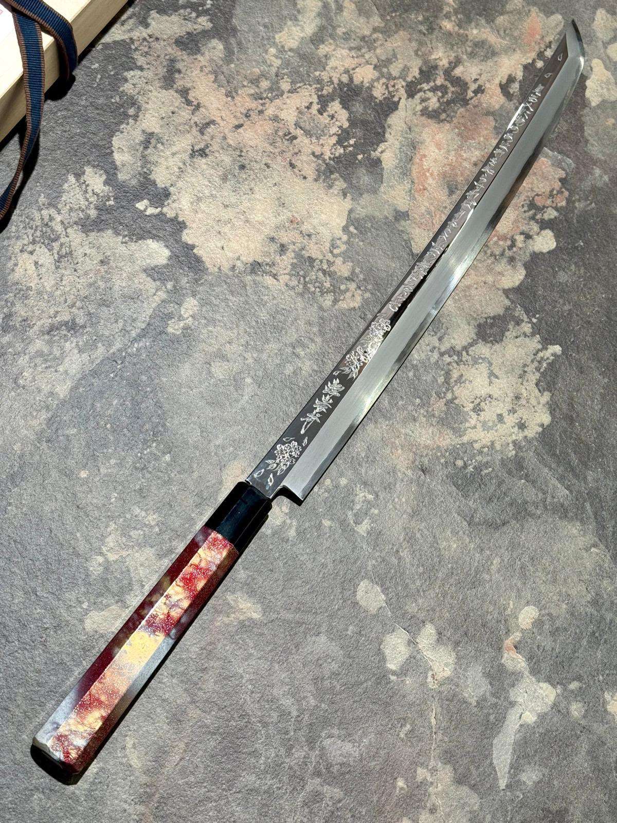 Cuchillo yanagiba de hoja larga con mango lacado apoyado en diagonal sobre una superficie de piedra